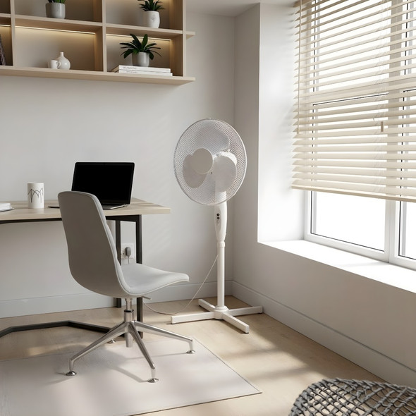 16 inch white oscillating pedestal fan beside a desk and laptop in a bright home office with window blinds
